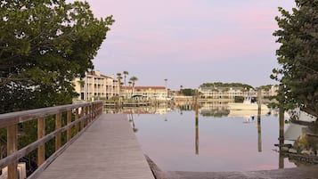 Eine hölzerne Promenade führt zu ruhigem Gewässer, im Hintergrund sind Gebäude zu sehen.