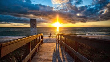Ein Holzsteg führt zum Meer, im Hintergrund ist ein Sonnenuntergang zu sehen.
