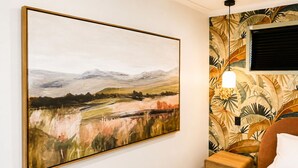 A bedroom with a large landscape painting, a bed with a white pillow, a nightstand, and a wall with a tropical leaf pattern. - Tropical retreat with pool, Mineral spa & games room! (Mudgeeraba)