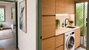 A modern kitchen with a built-in washing machine, wooden cabinets, and a small sink. - Tropical retreat with pool, Mineral spa & games room! (Mudgeeraba)