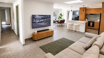 A modern living room with a flat-screen TV, a sofa, and a dining area with a bar.