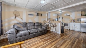 A modern living room with a grey sofa, wooden flooring, and a kitchen area with white cabinets and a microwave. - Beach Cabin #1, Private/Shared Beach - Cabin #1 (Lake Ozark)