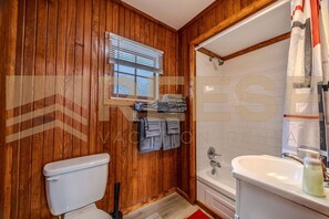 Une salle de bain aux murs lambrissés, équipée de toilettes, d’un lavabo et d’une douche.