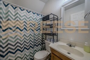 A bathroom with a chevron-patterned shower curtain, a white toilet, a sink with a mirror, and a towel rack with folded towels. - Large Beach Cabin, Private/Shared Beach Family Cabin (Lake Ozark)