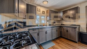 A modern kitchen with dark wood cabinets, a gas stove, and a large window. - Mid-Century Cabin, Pet Friendly Mid-Century Cabin (Lake Ozark)