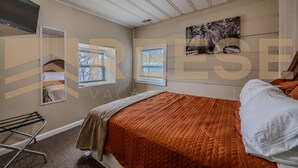 A bedroom with a bed, a window, a mirror, and a wall-mounted TV. - Mid-Century Cabin, Pet Friendly Mid-Century Cabin (Lake Ozark)