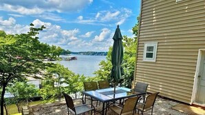 A patio with a table and chairs, overlooking a body of water with boats, trees, and a building with a door. - Mid-Century Cabin, Pet Friendly Mid-Century Cabin (Lake Ozark)