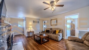 A spacious living room with a wooden floor, a ceiling fan, a sofa, and a coffee table. - Mid-Century Cabin, Pet Friendly Mid-Century Cabin (Lake Ozark)