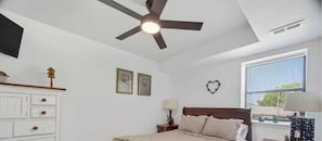 A bedroom with a bed, a ceiling fan, a window with blinds, a dresser, and wall decorations.