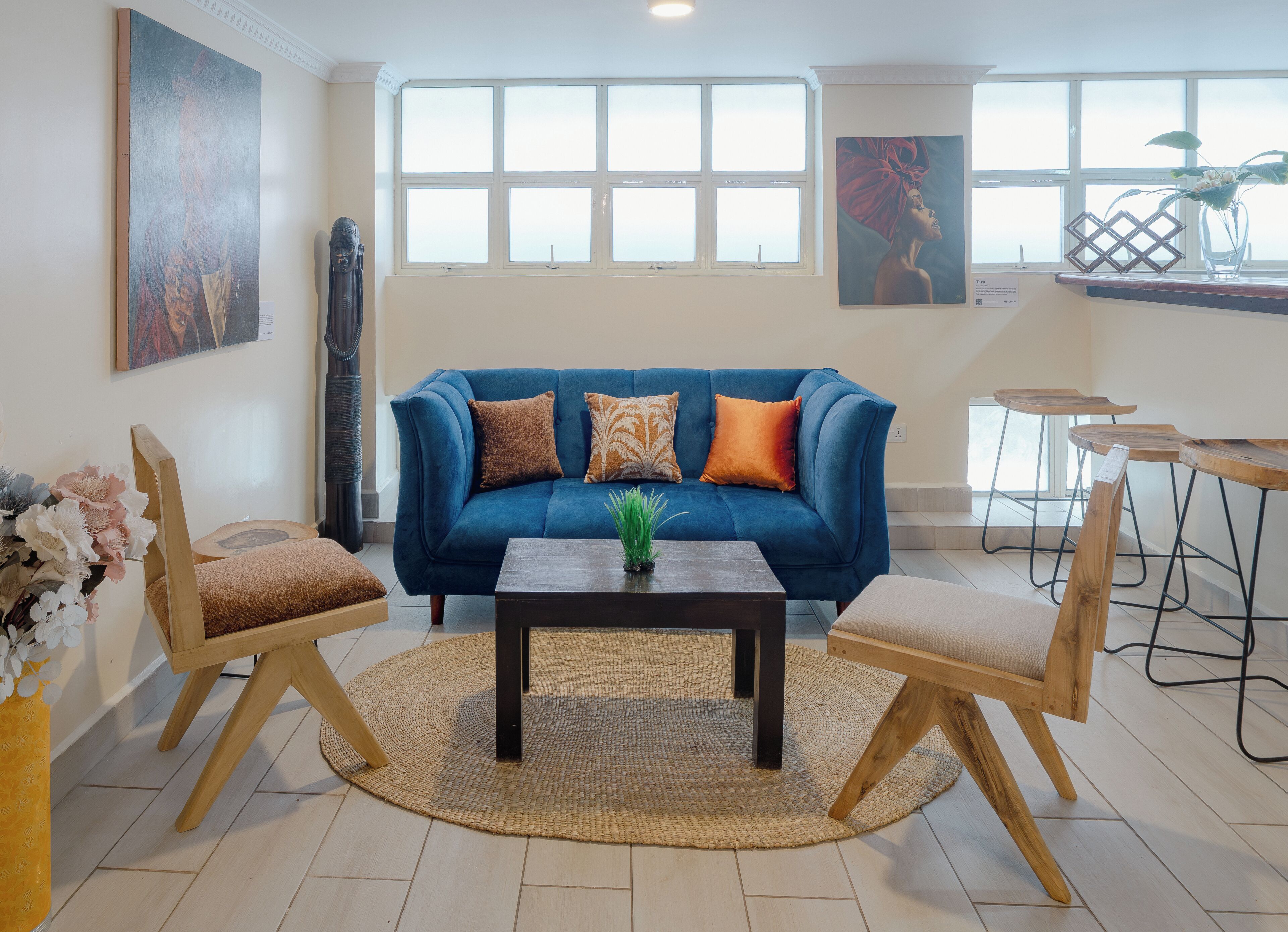 Ein Wohnzimmer mit einem blauen Sofa, zwei Holzstühlen, einem Couchtisch und einem großen Fenster mit vielen Sprossen.