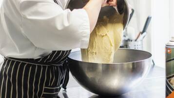 A person in a white shirt and striped apron handling a large metal mixing bowl.