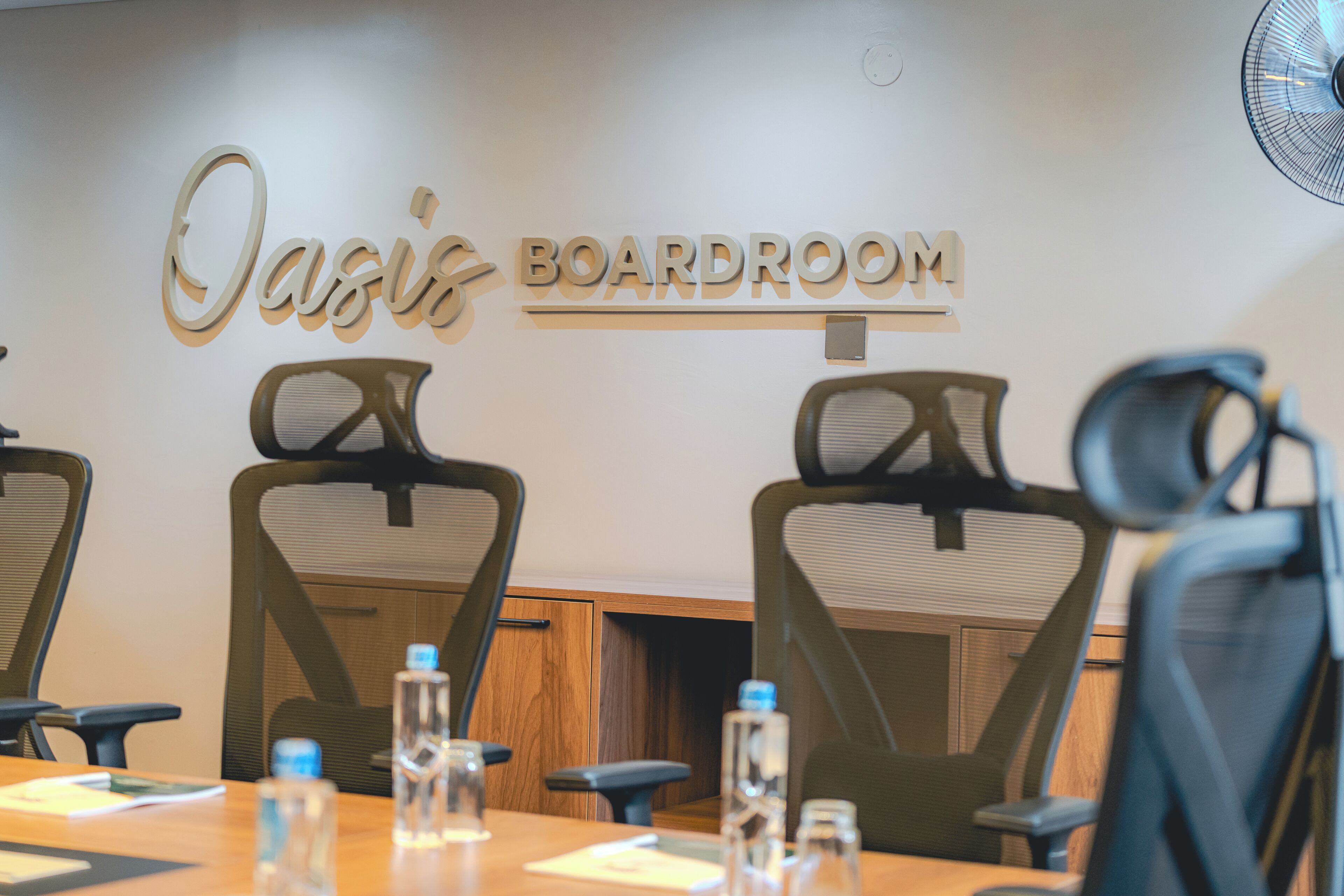 A conference room with a sign reading 'Oasis Boardroom,' equipped with chairs and tables, and water bottles on the table.