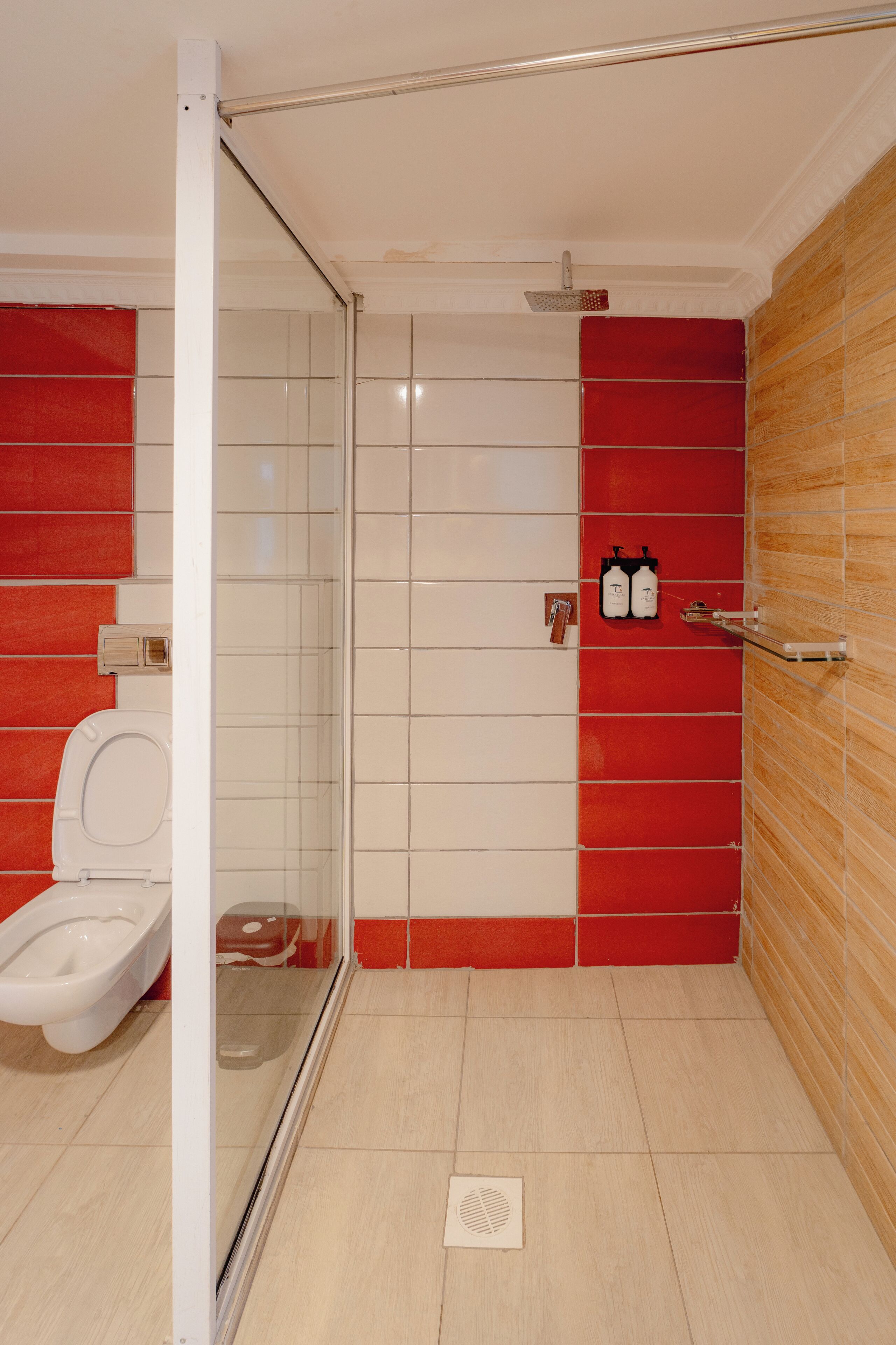 Ein Badezimmer mit Duschkabine aus Glas, Toilette und einer Wand mit roten und weißen Fliesen.