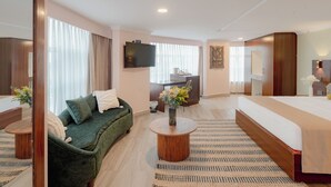 A hotel room with a bed, a green sofa, a round wooden coffee table, a TV, and a desk with a chair. - Karen Plains Hotel (Nairobi)