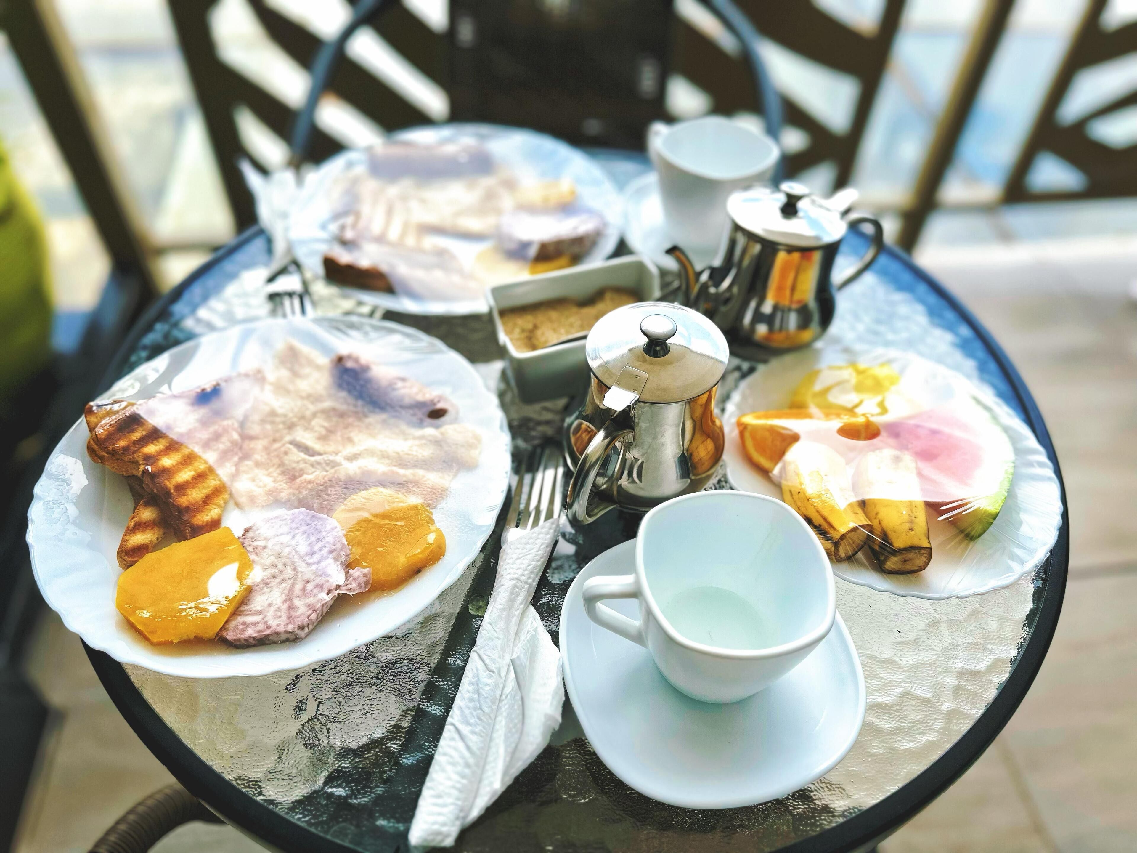 Une table mise pour le petit-déjeuner, avec des assiettes remplies de nourriture, une cafetière et une tasse.