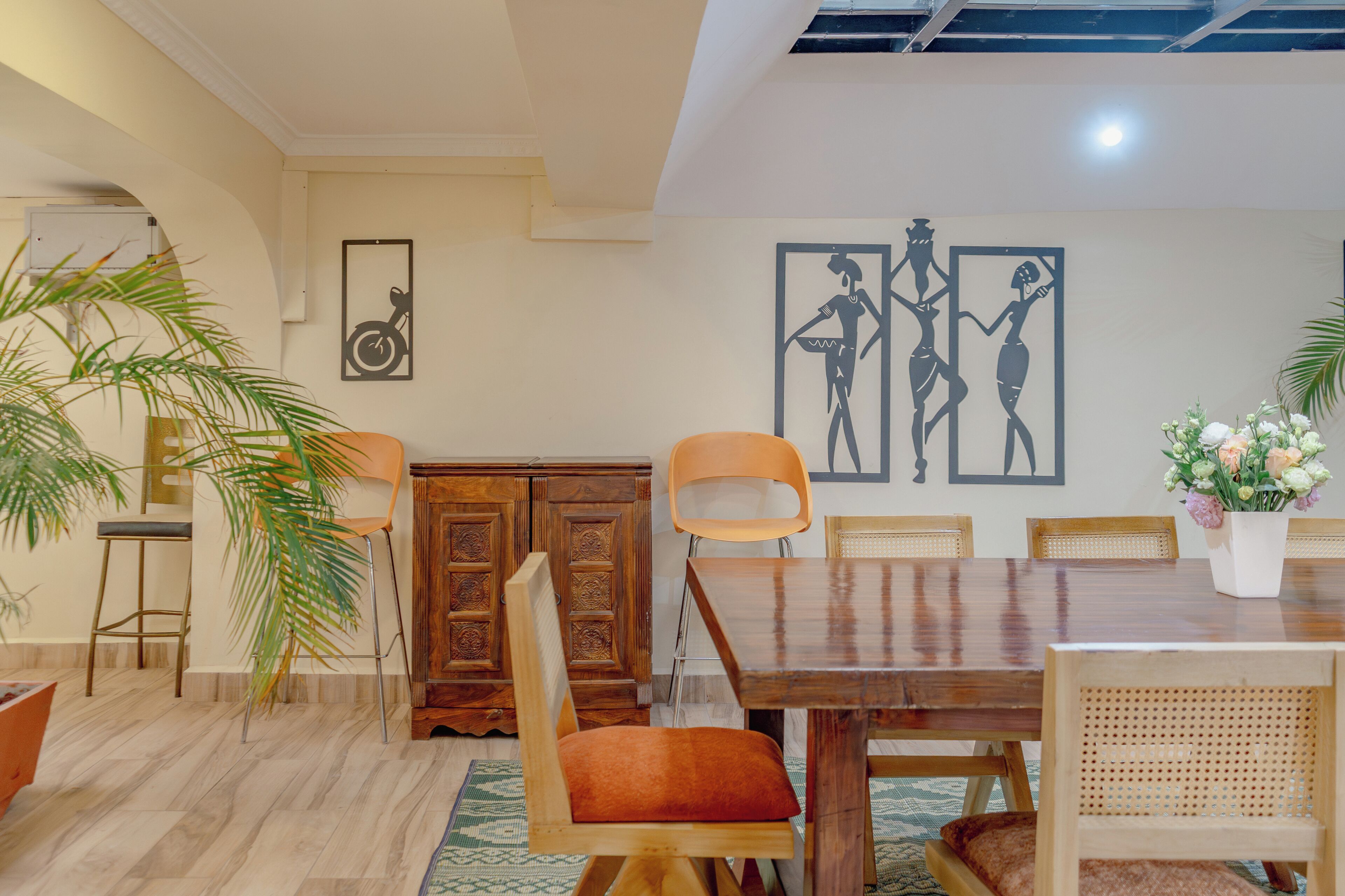 Un comedor con una mesa de madera, sillas, una planta en maceta y obras de arte en la pared.