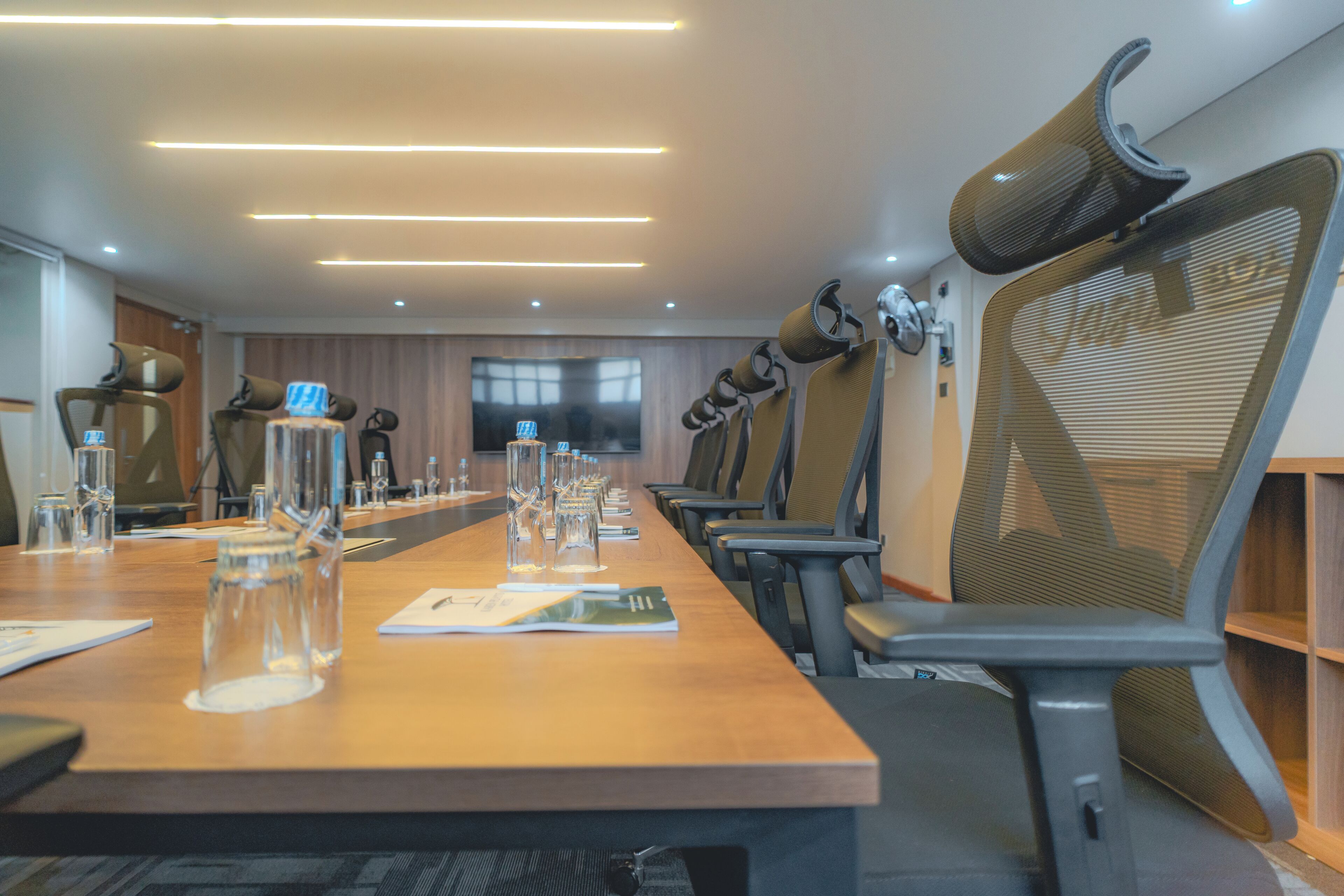 Une salle de conférence avec une longue table, des chaises et un écran de télévision.
