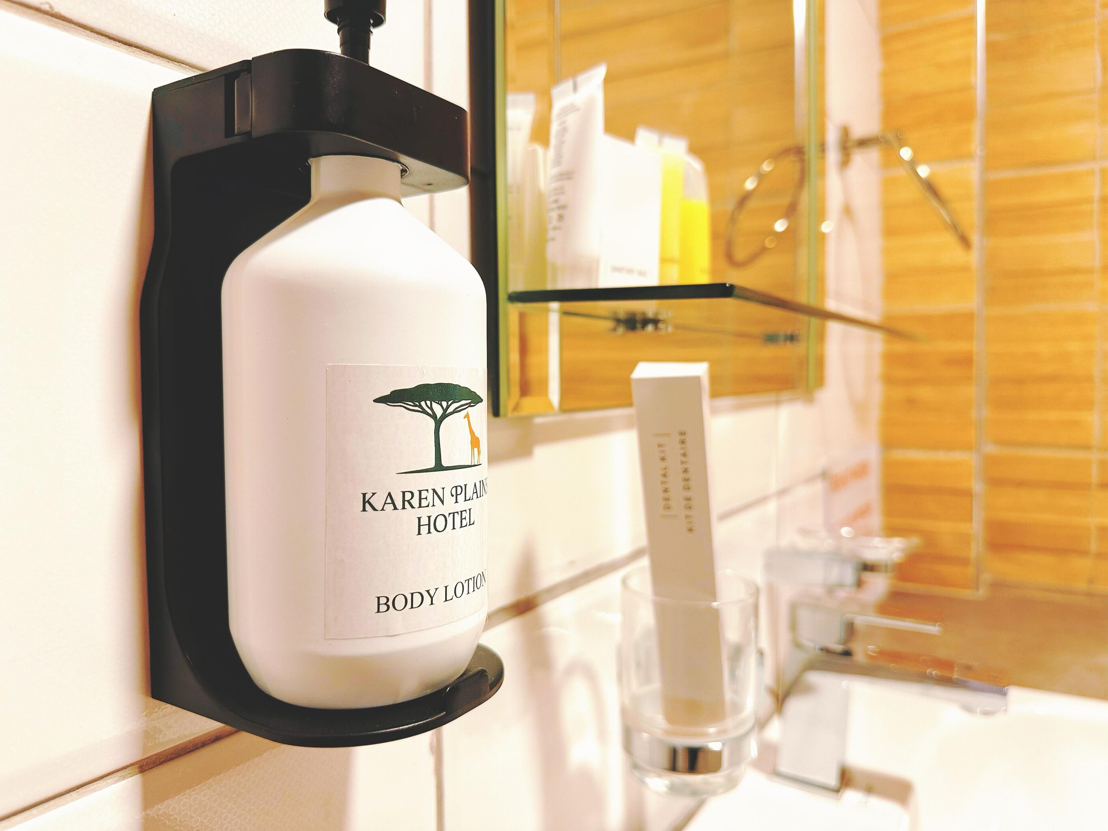 A hotel bathroom with a body lotion dispenser, a glass soap dispenser, and a mirror.