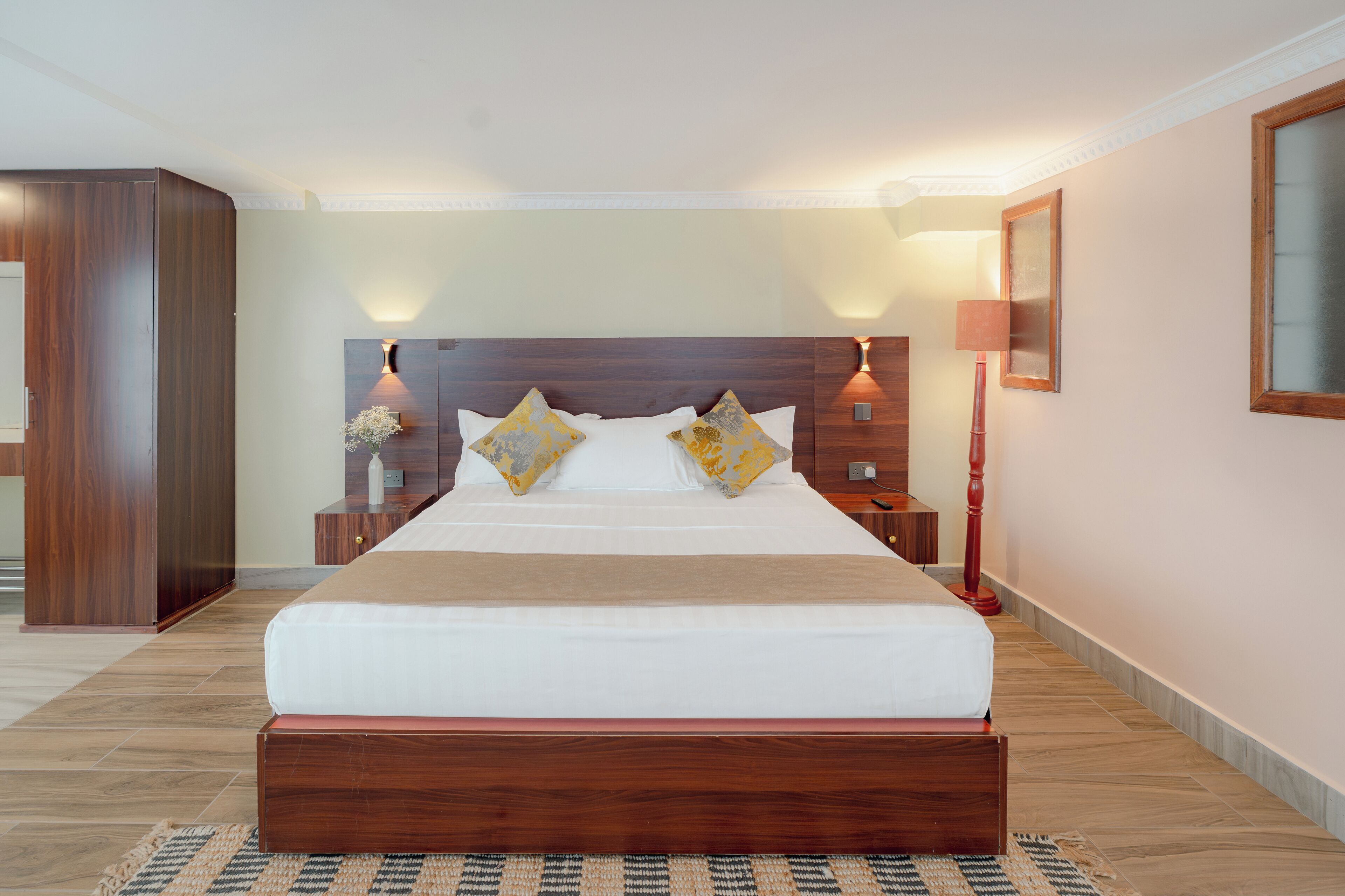 A hotel room with a large bed, wooden headboard, bedside tables, and a nightstand with a lamp.