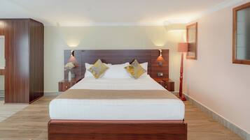 A hotel room with a large bed, wooden headboard, bedside tables, and a nightstand with a lamp.