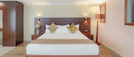 A hotel room with a large bed, wooden headboard, bedside tables, and a nightstand with a lamp.