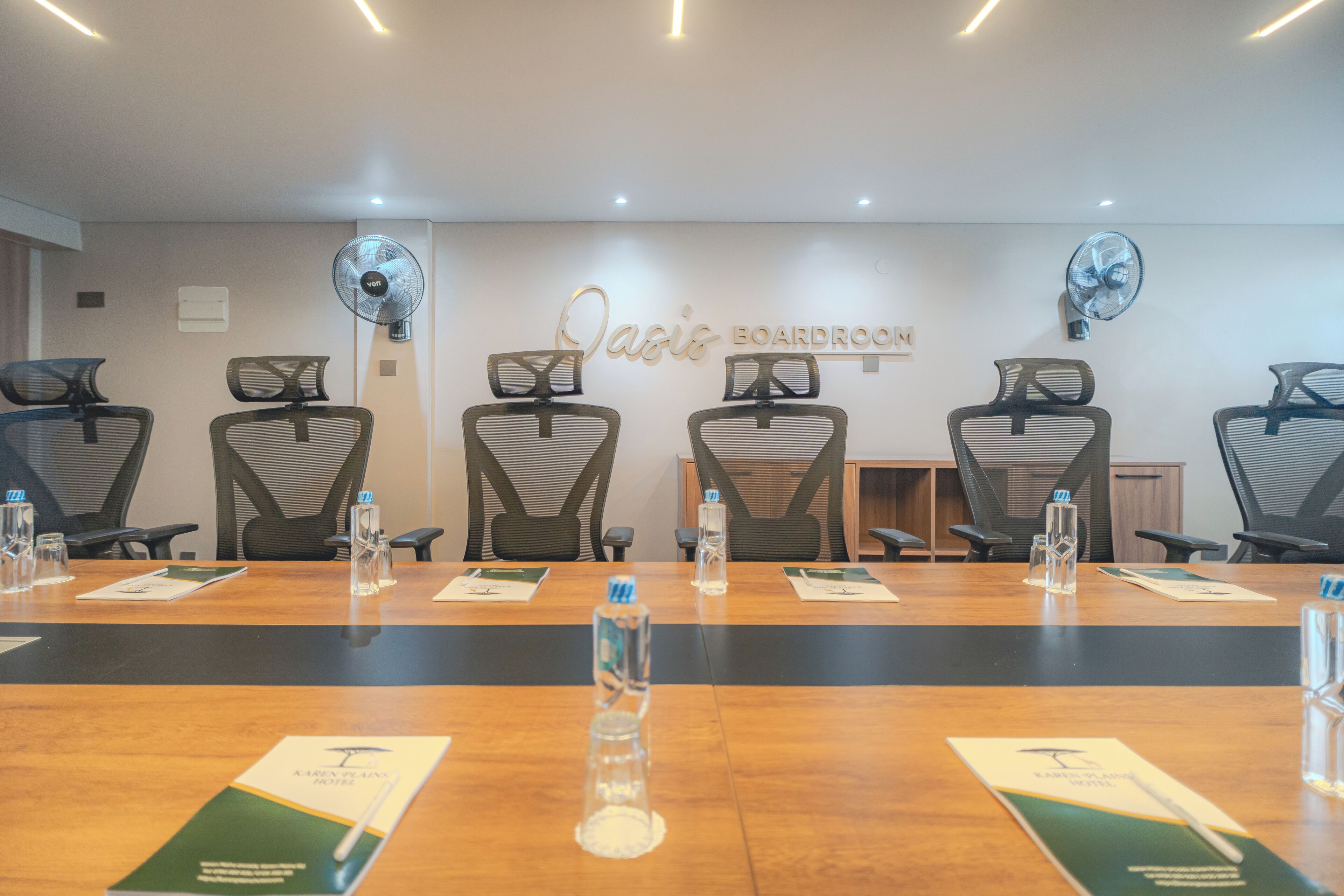 A conference room with a long table, multiple chairs, and two wall-mounted fans.