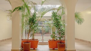 A corridor with large potted plants, arched ceilings, and a view through glass doors. - Karen Plains Hotel (Nairobi)
