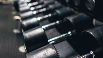 A row of black dumbbells in a gym with a metal ceiling and visible structural beams.