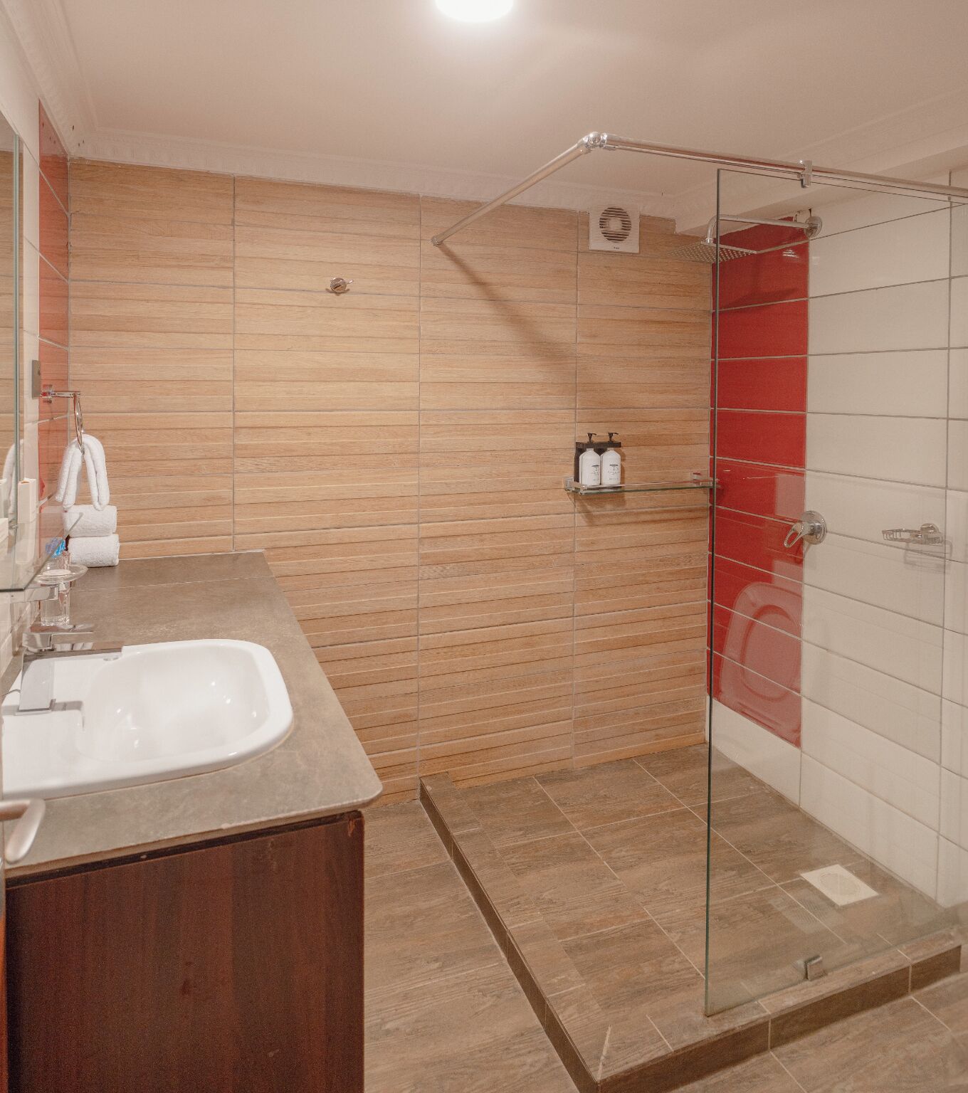 A modern bathroom with a glass shower enclosure, a wooden vanity, and a tiled floor.
