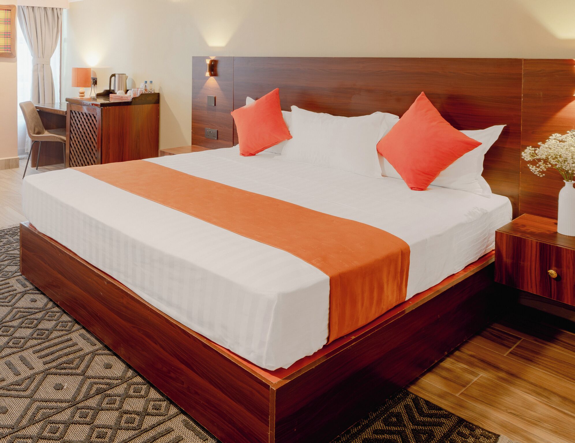 A hotel room with a large bed, wooden headboard, bedside tables, a desk, and a chair.