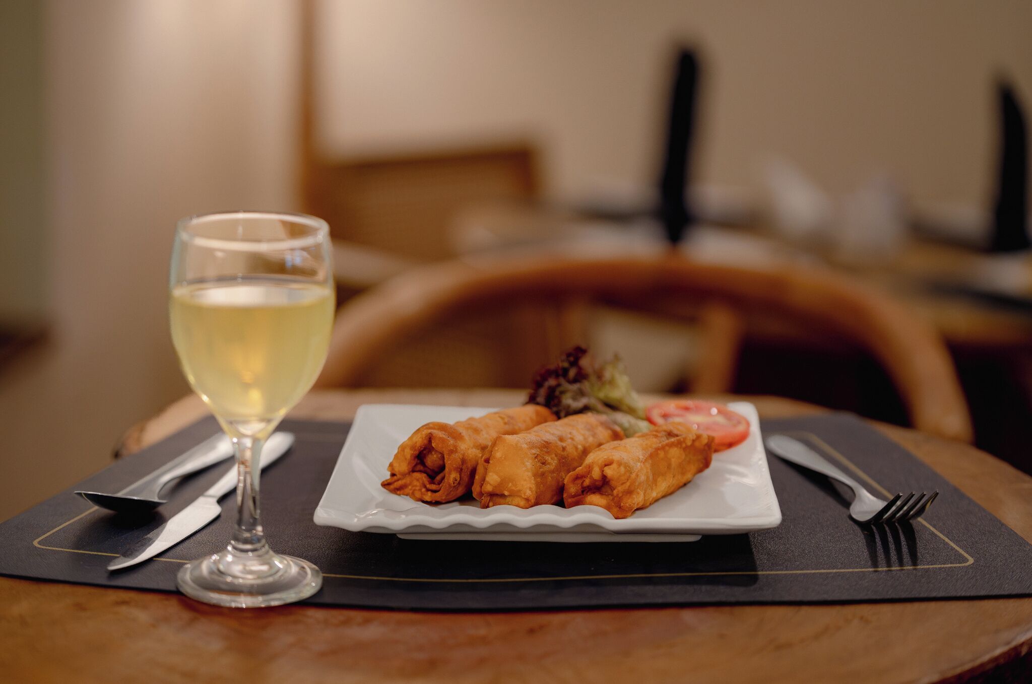 Une table à manger avec une assiette de nourriture, un verre de vin blanc et des couverts.
