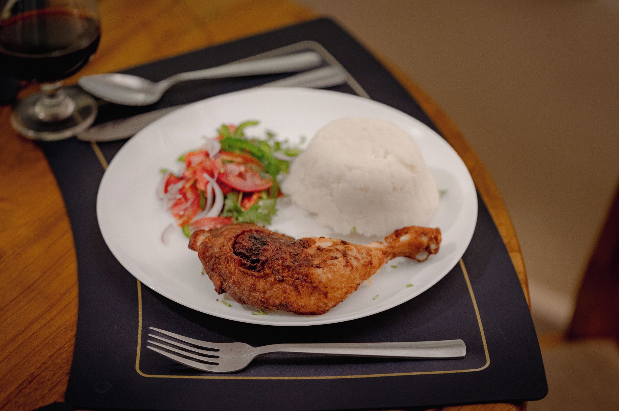 A plate with a fried chicken leg, a mound of white rice, and a side salad on a dark placemat.