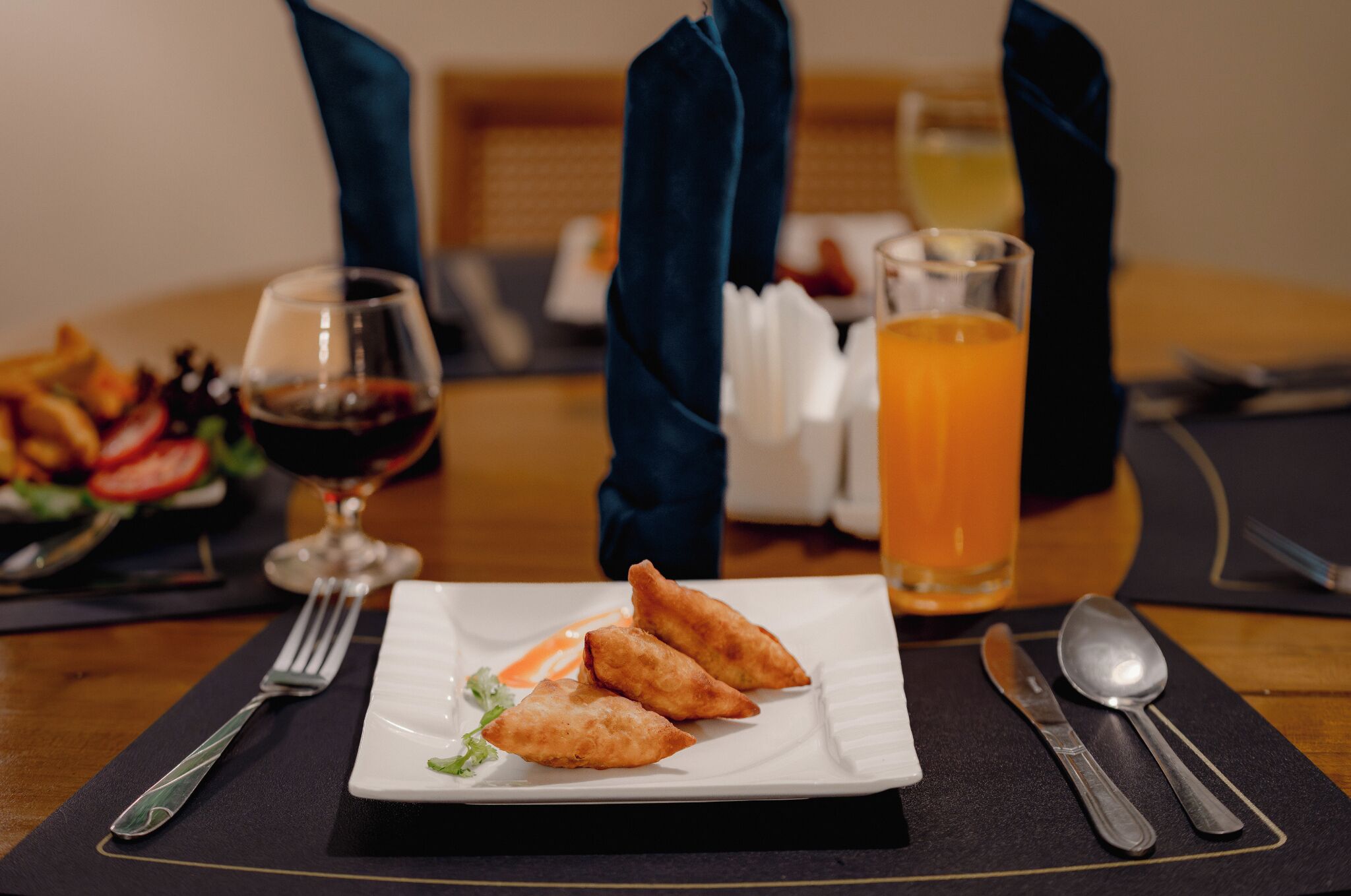 A dining table with a plate of food, a glass of red wine, a glass of orange juice, and cutlery.