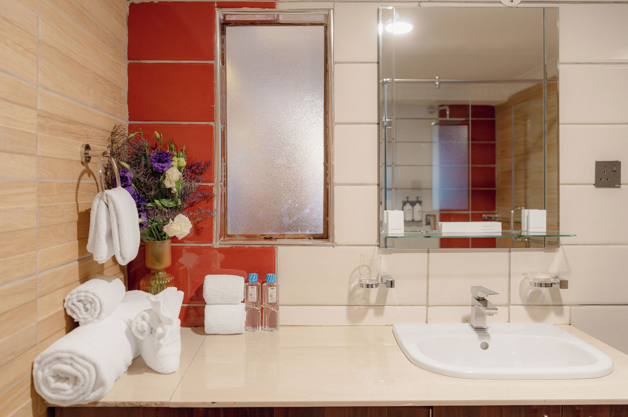 A bathroom with a large mirror, a sink, towels, and toiletries.