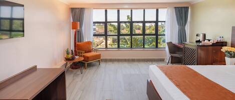 Habitación de hotel con cama, escritorio, silla y ventanas amplias que ofrecen vistas al exterior.