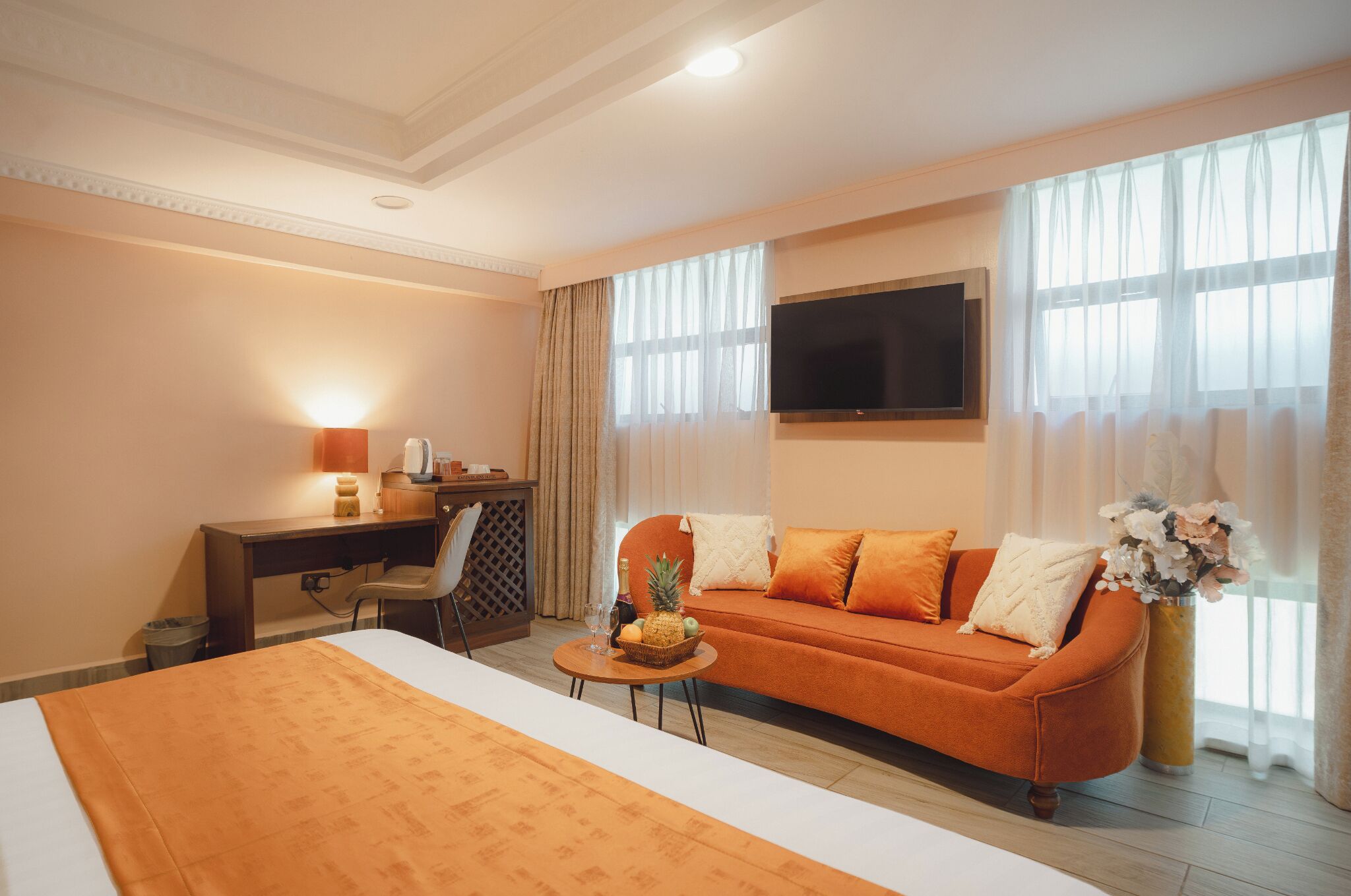 A hotel room with a bed, a sofa, a desk, a TV, and a window with curtains.