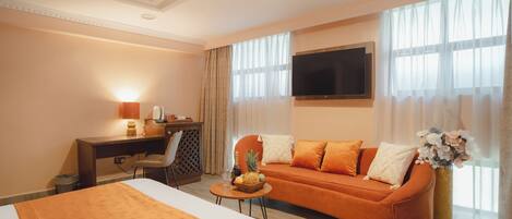 A hotel room with a bed, a sofa, a desk, a TV, and a window with curtains.