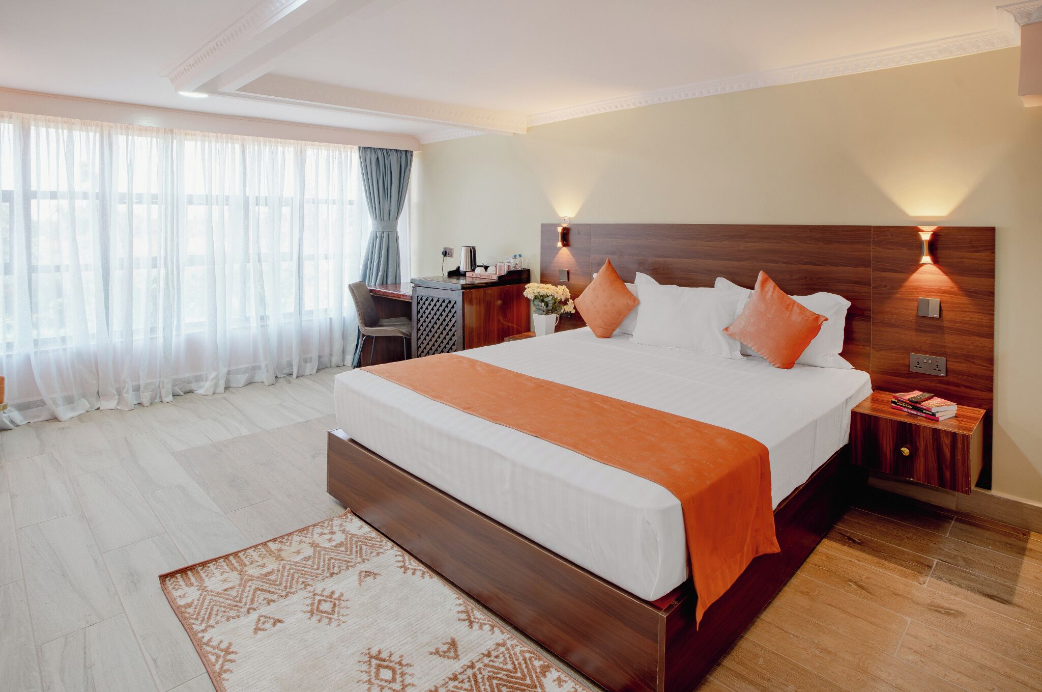 Une chambre d’hôtel avec un grand lit, un bureau, une chaise, une table de chevet et une fenêtre avec des rideaux légers.