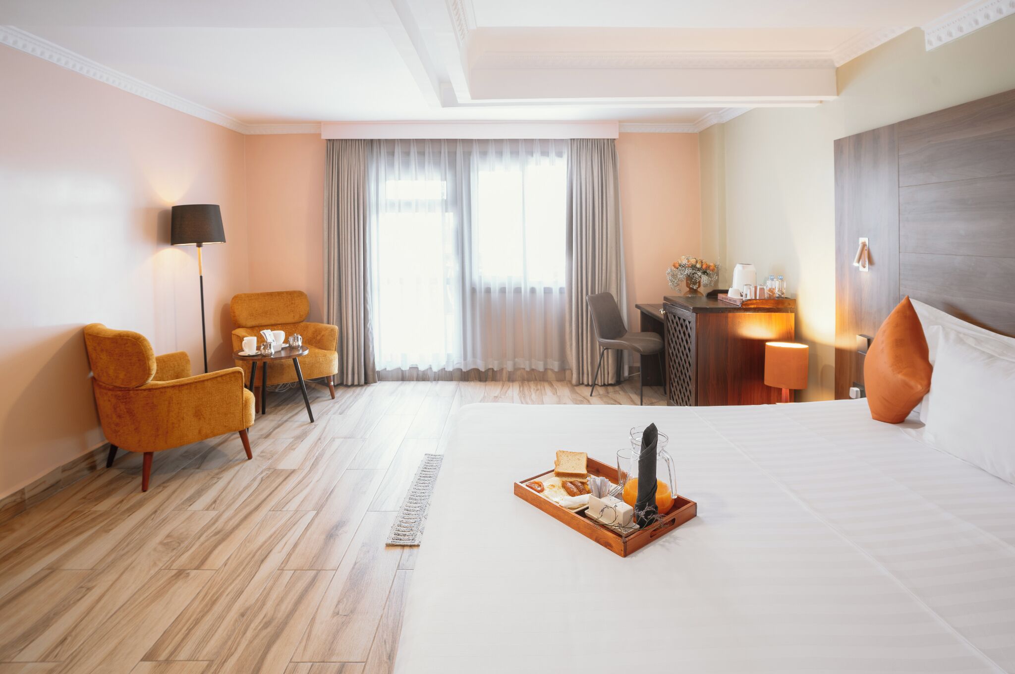 A hotel room with a bed, a desk, a chair, a lamp, and a window with curtains.