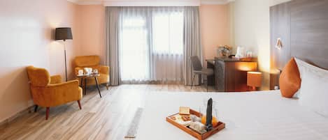 Habitación de hotel con cama, escritorio, silla, lámpara y ventana con cortinas.