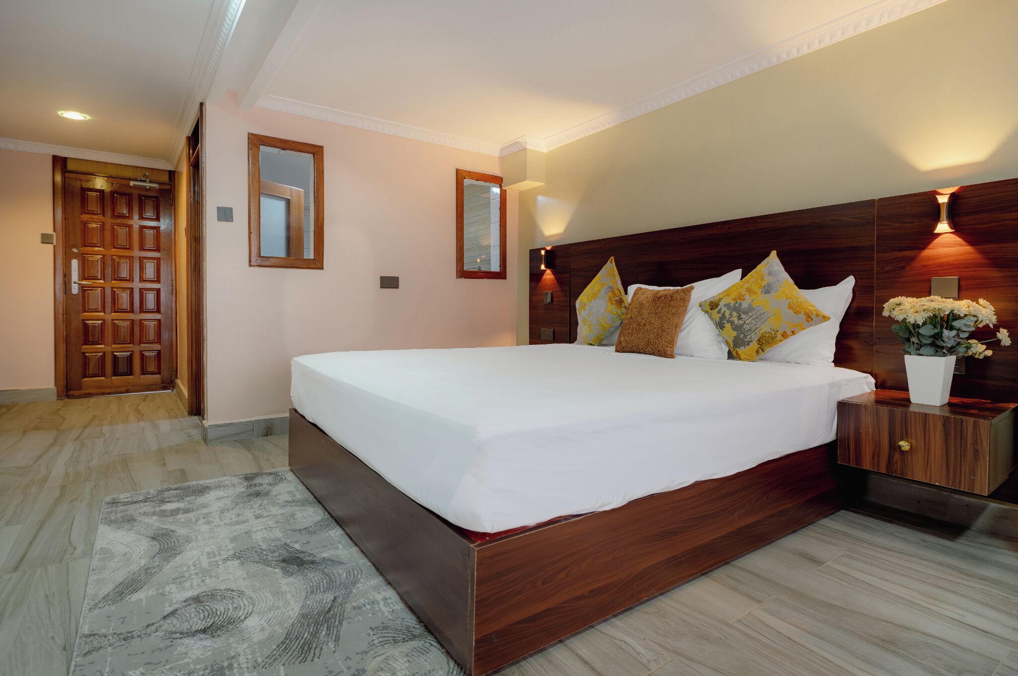 A bedroom with a wooden bed, bedside tables, a mirror, and a nightstand with a vase of flowers.
