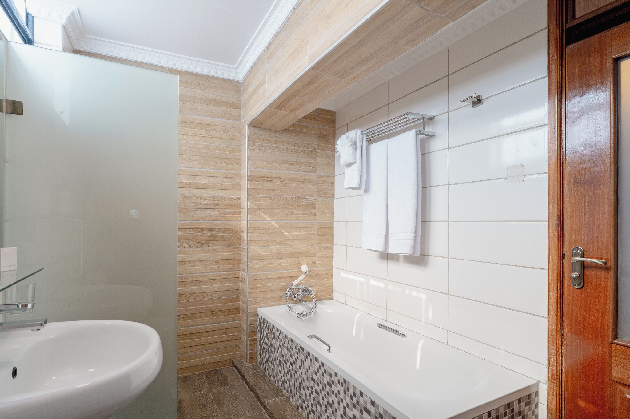 Une salle de bain moderne avec une douche à parois de verre, un lavabo blanc, une baignoire et une porte en bois.