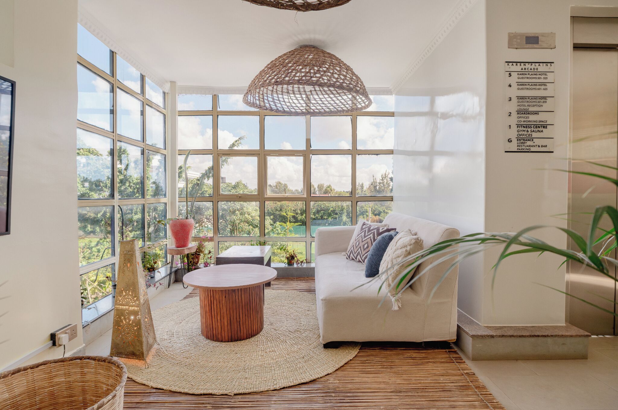 A spacious room with large windows, a white sofa, a round coffee table, and a hanging light fixture.