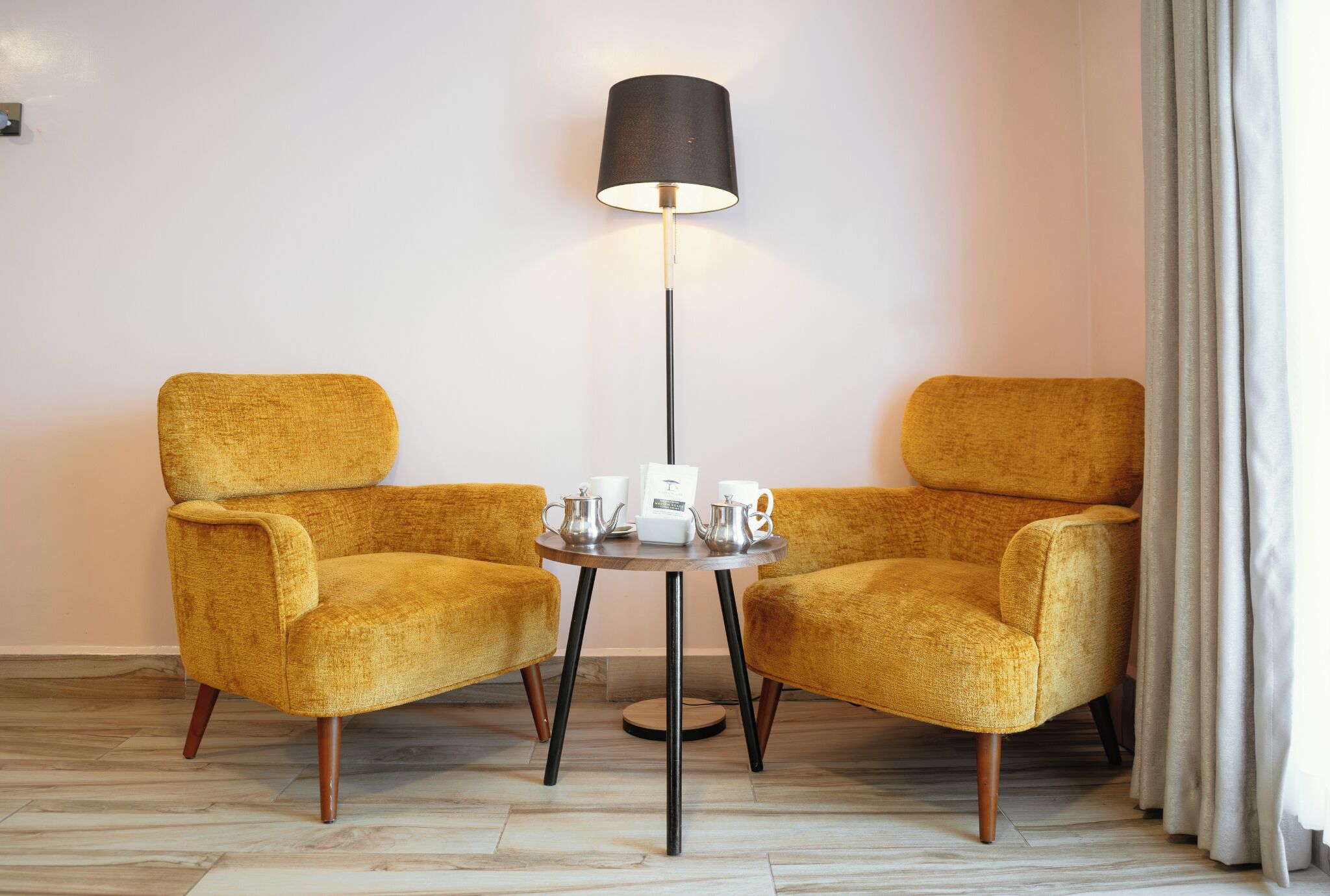 A room with two yellow armchairs, a small round table with a lamp, and a white wall.
