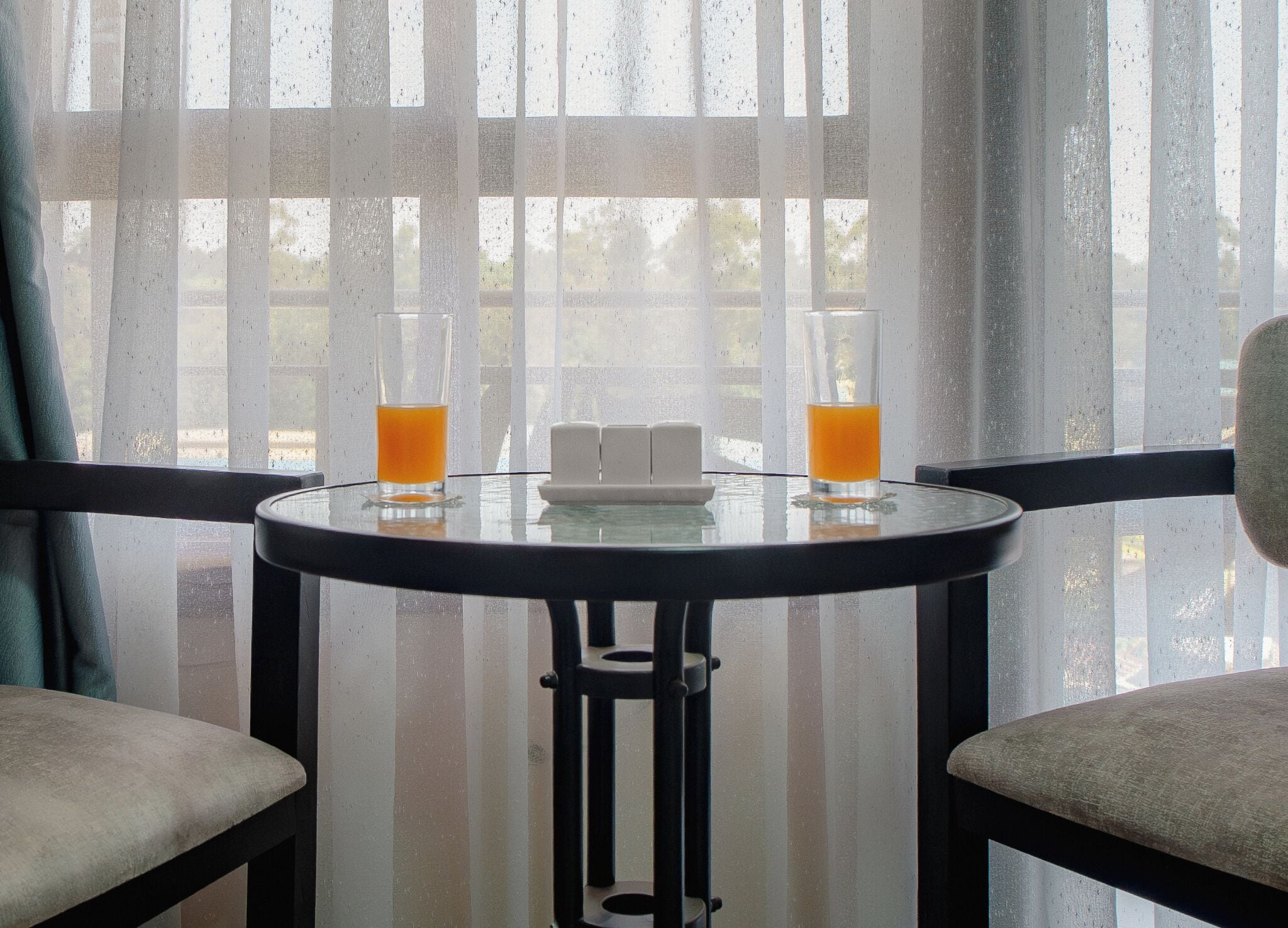 Ett runt glasbord med två glas apelsinjuice, en liten vit tallrik samt salt- och pepparkar.