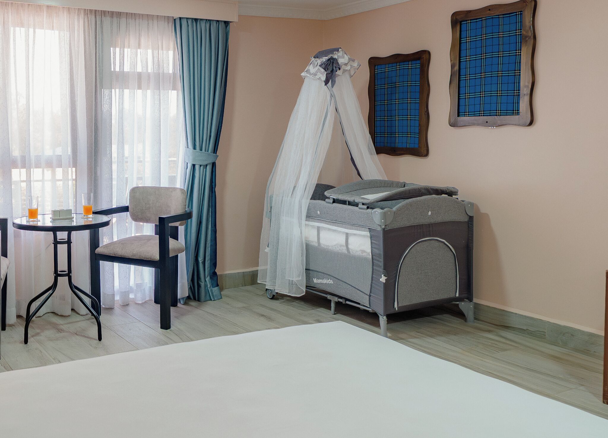 A room with a bed, a chair, a table with two glasses of orange juice, and a baby crib with a canopy.