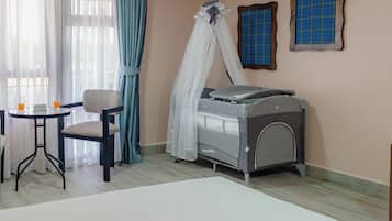A room with a bed, a chair, a table with two glasses of orange juice, and a baby crib with a canopy.
