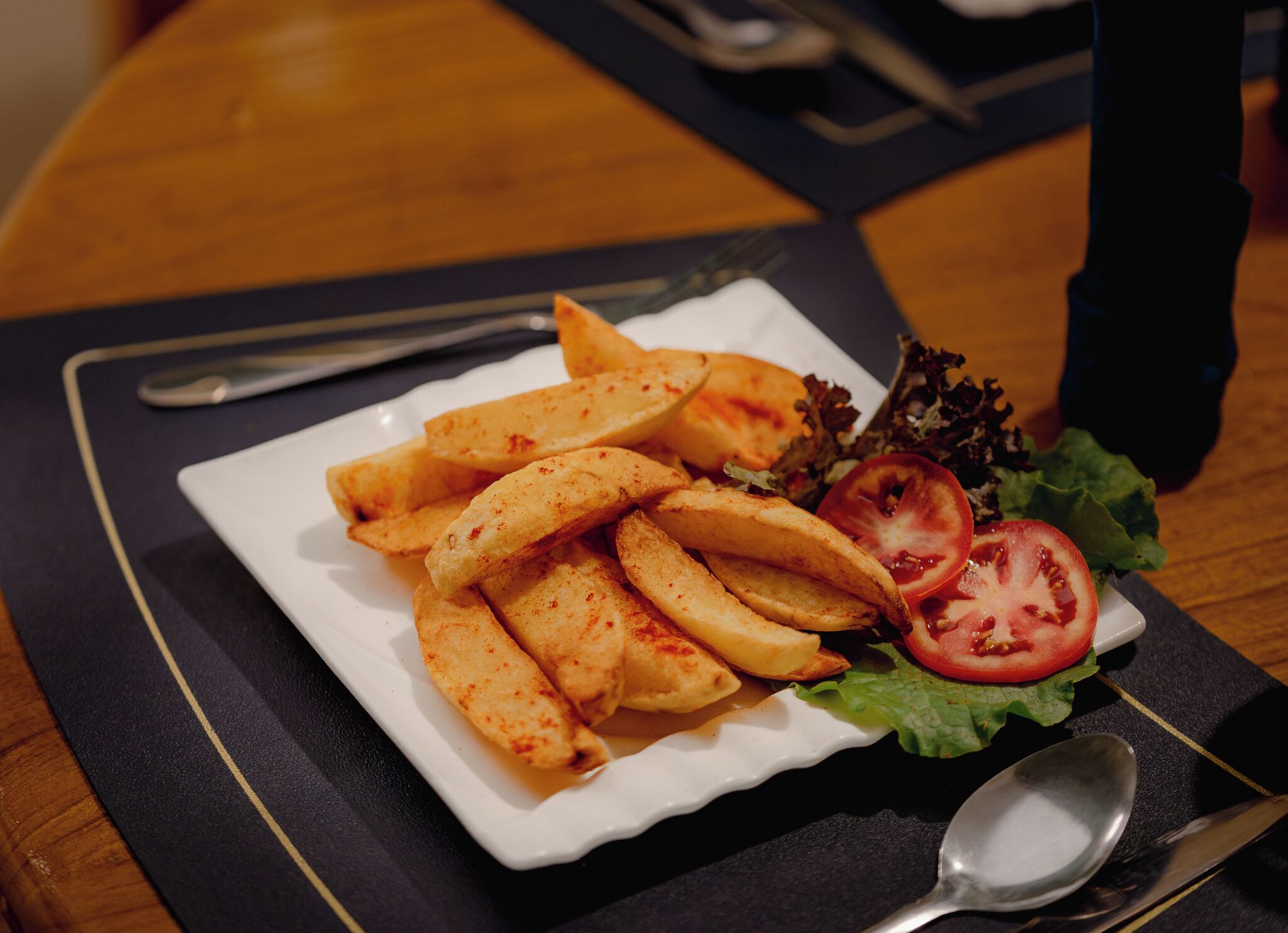 A plate of seasoned potato wedges with a side salad and a slice of tomato on a white plate.
