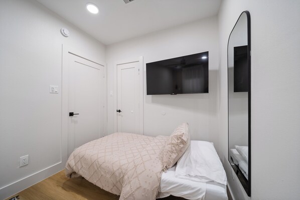 Une chambre à coucher avec un lit, un téléviseur à écran plat fixé au mur et une porte.