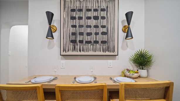 Un coin repas avec une table en bois dressée pour quatre personnes, deux appliques murales et une plante en pot posée sur la table.